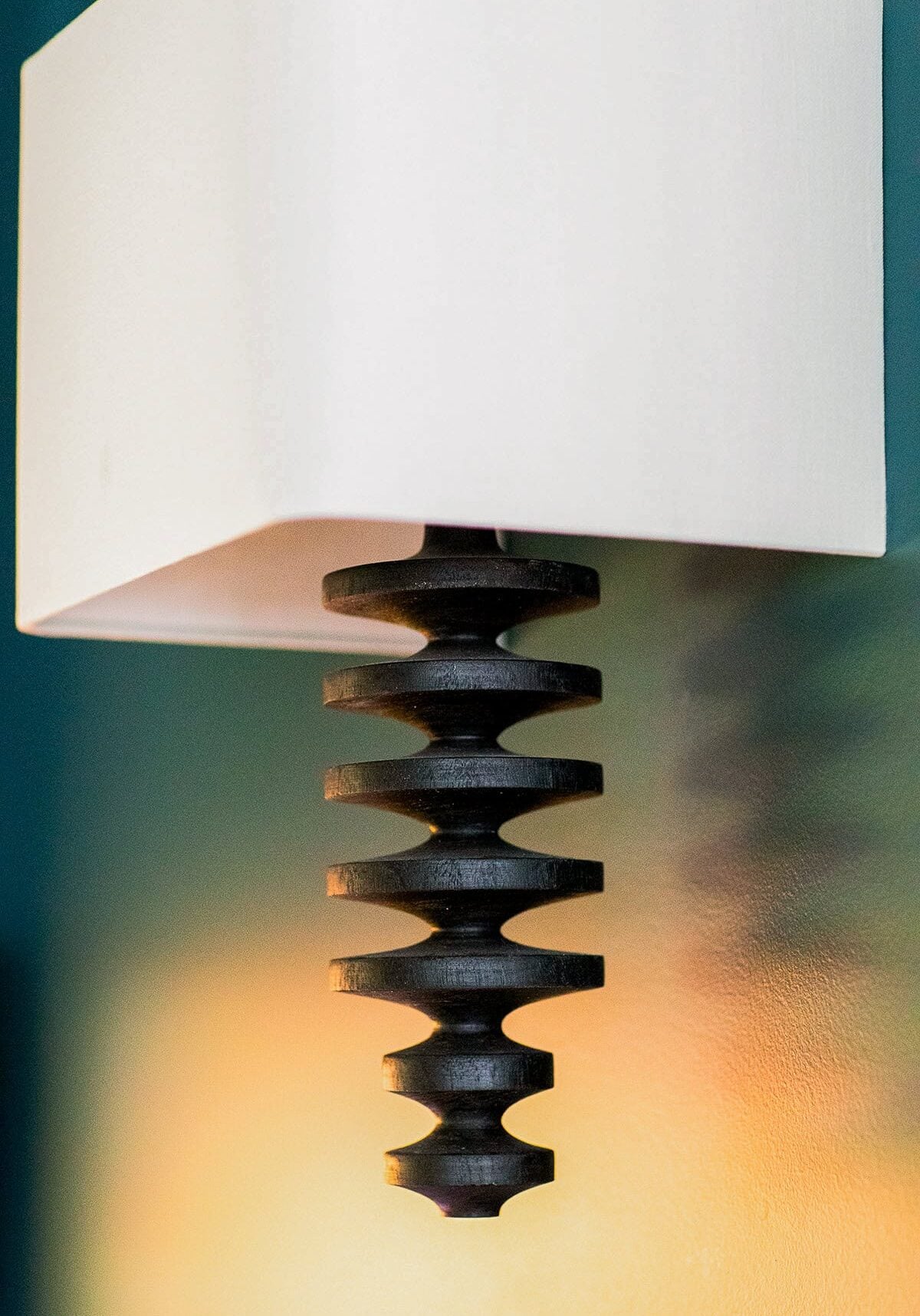 A modern wall-mounted light fixture with a white rectangular shade and a spiral, ridged black metal accent casting shadows on the wall.