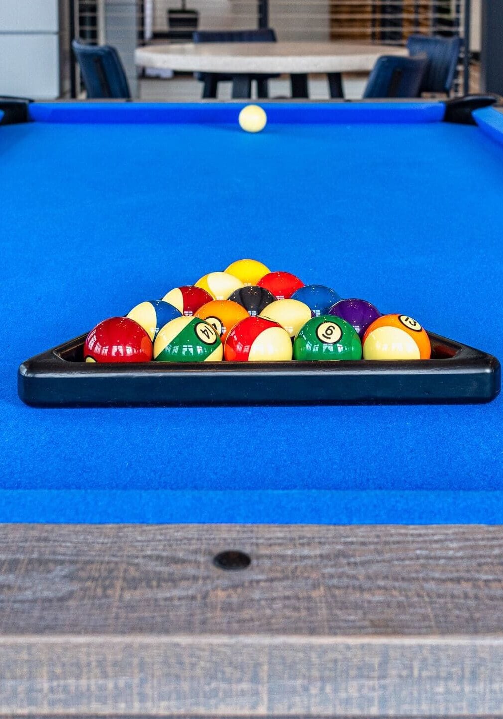 A blue pool table with racked billiard balls in the center and a cue ball positioned at the far end.