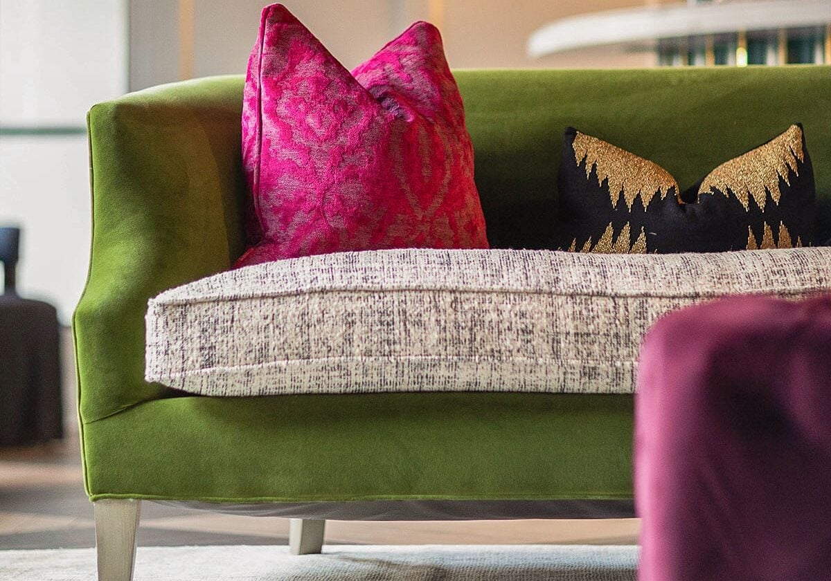 Close-up of a luxury commercial settee featuring green velvet, performance weave seat cushions, and custom damask and gold-embroidered accent pillows.