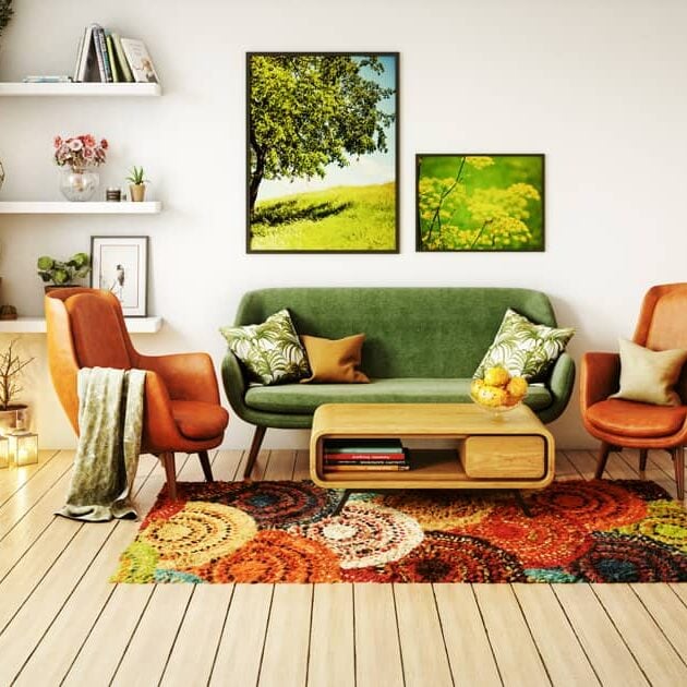 A bright living room by Crimson Design Group features orange chairs, a green sofa, a colorful rug, wall art, shelves with décor, and wood flooring.