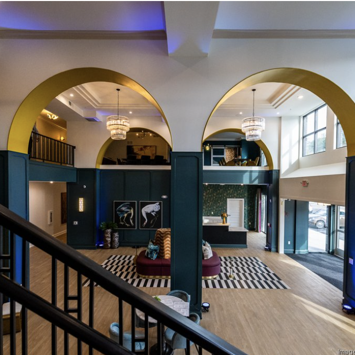 A modern lobby by Crimson Design Group with high ceilings, large arched doorways, lounge seating, decorative lighting, and a staircase in the foreground.