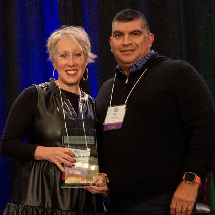 Two people from Crimson Design Group stand side by side at an event; the woman is holding a glass award and both are wearing conference name badges.